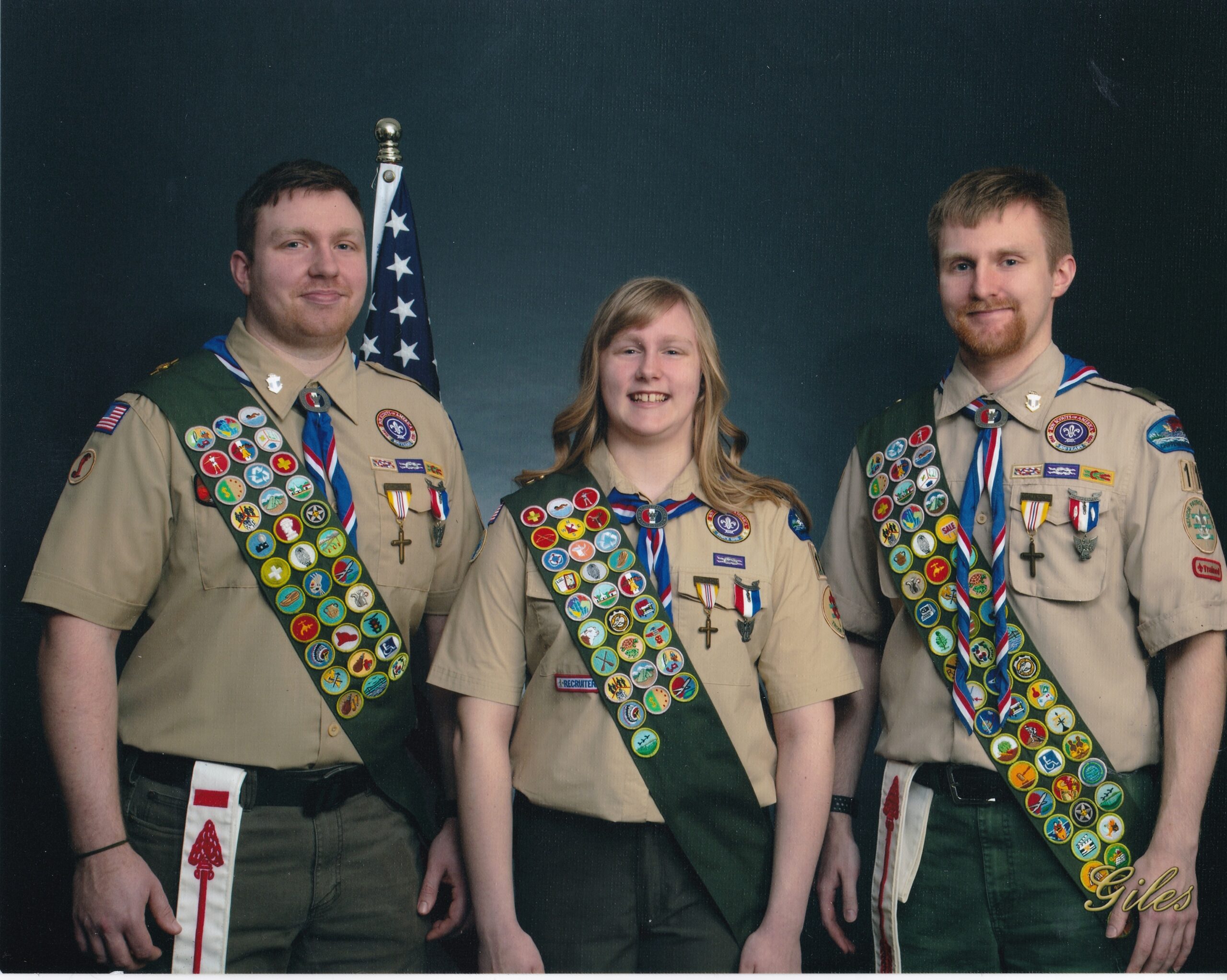 Alyxandria stands with her two brothers on either side of her. They all are wearing Eagle Scout uniforms showing their medals and many badges.