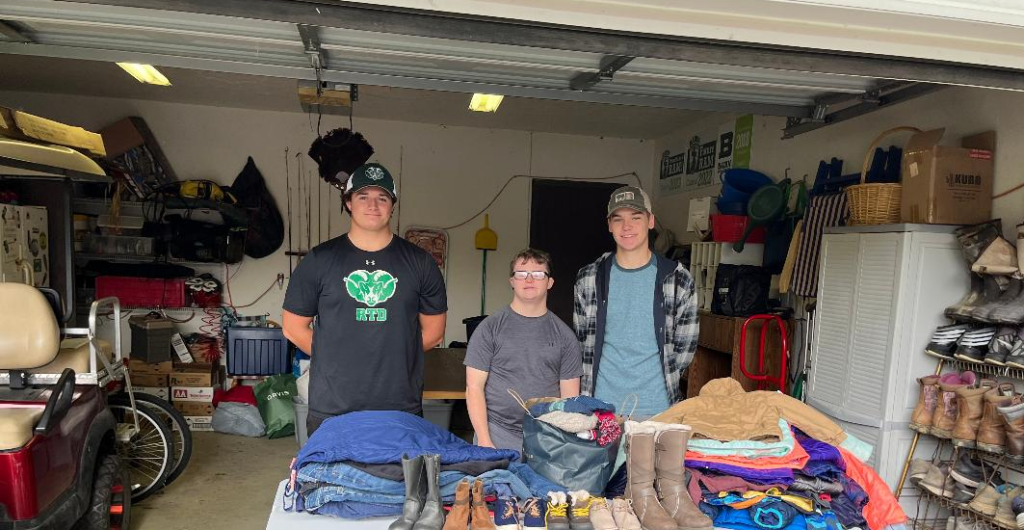 High school students standing in a garage, posing with bags of clothes from their clothing donation drive.