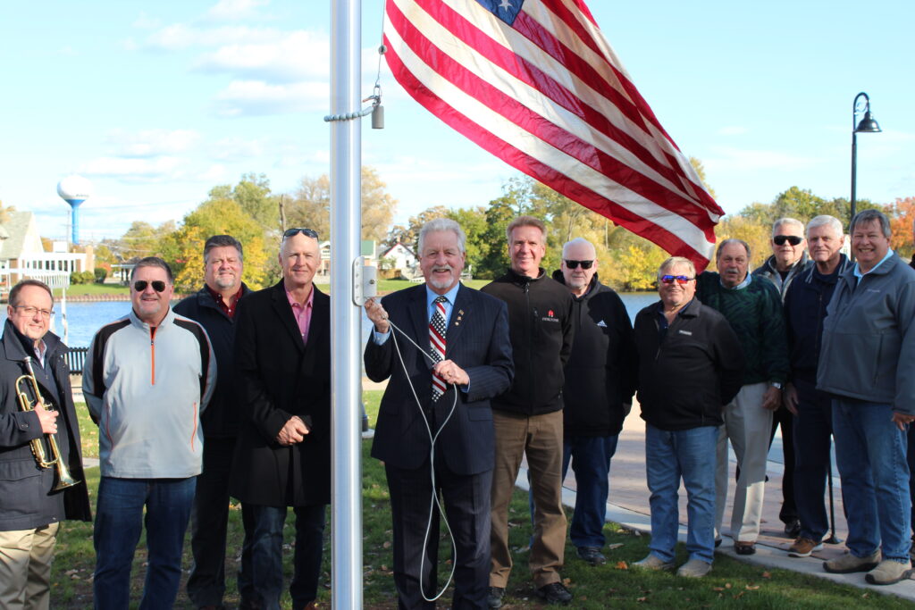 A group of men stand around a flagpole as one of the men raises the American flag. 