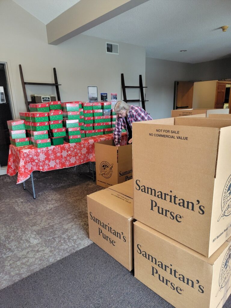 A woman fills large boxes with shoe boxes that contain donations. 