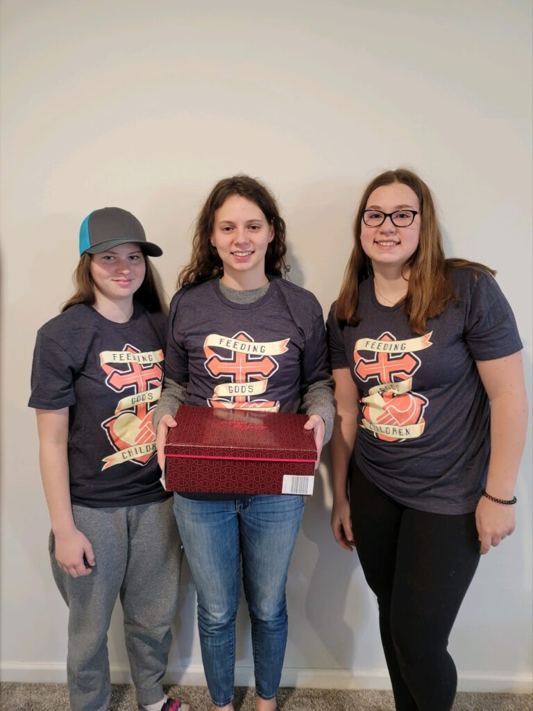 Three female student volunteers pose with one of the filled shoe boxes.