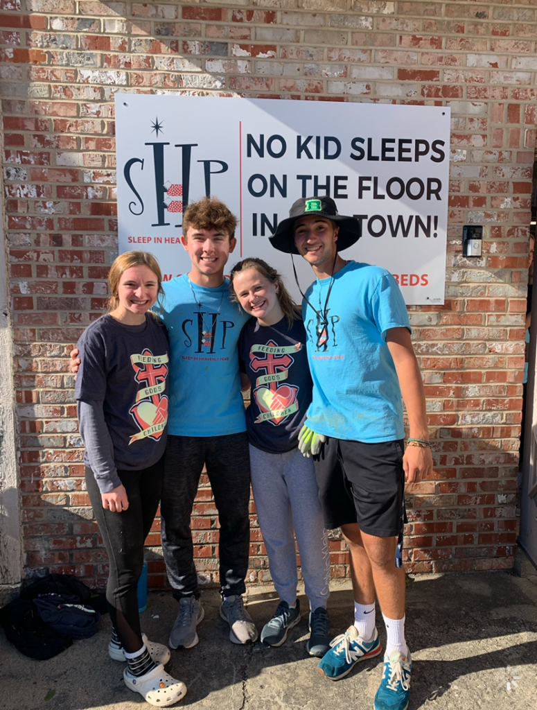 Four young volunteers pose in front of the Sleep in Heavenly Peace building.