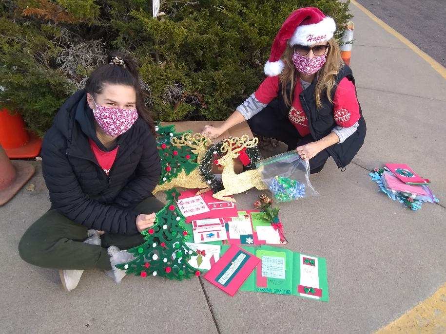 Two volunteers are shown with the hand crafted Christmas cards and decorations such as artwork of Christmas trees, a wreath, and reindeer. 