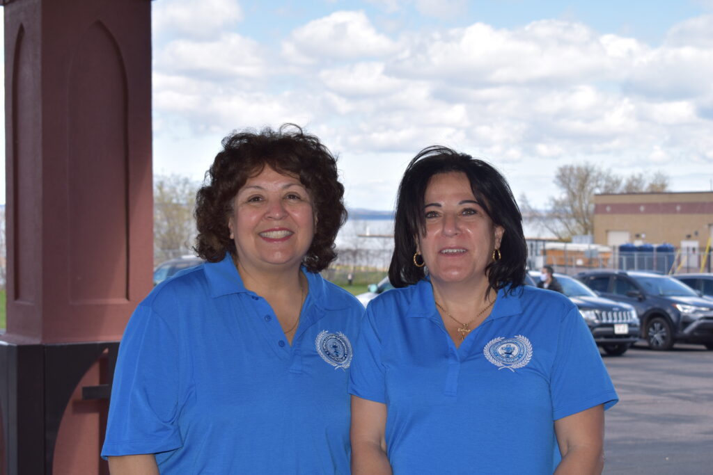 Two women wearing blue t-shirts with the Catholic Order of Foresters logo stand in a parking lot. 