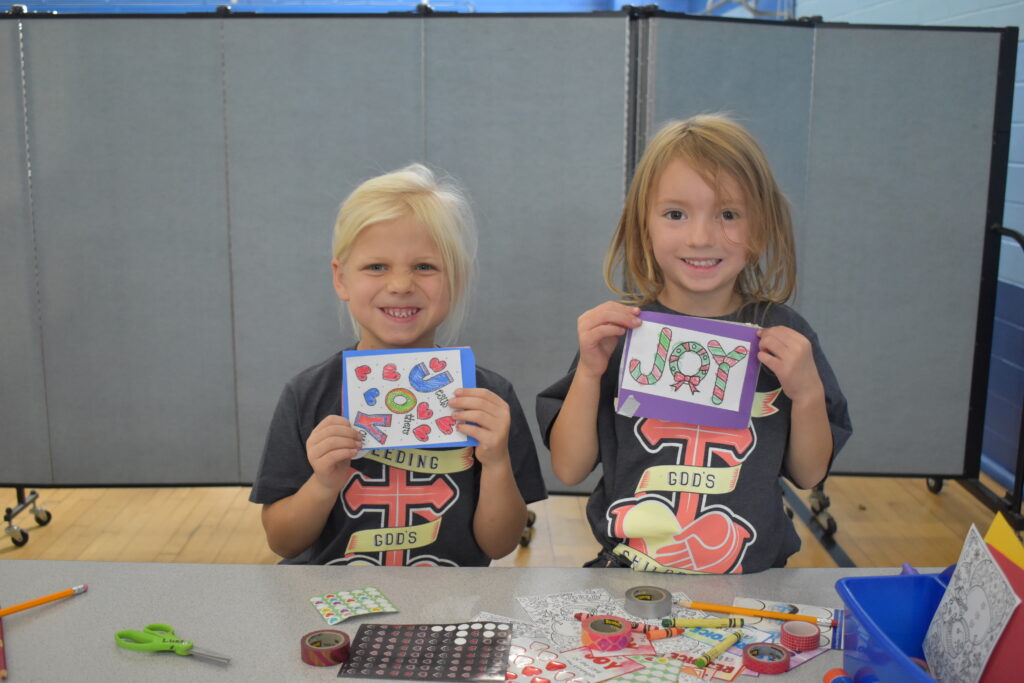 Two girls showing the greeting cards they crafted for the care boxes. 
