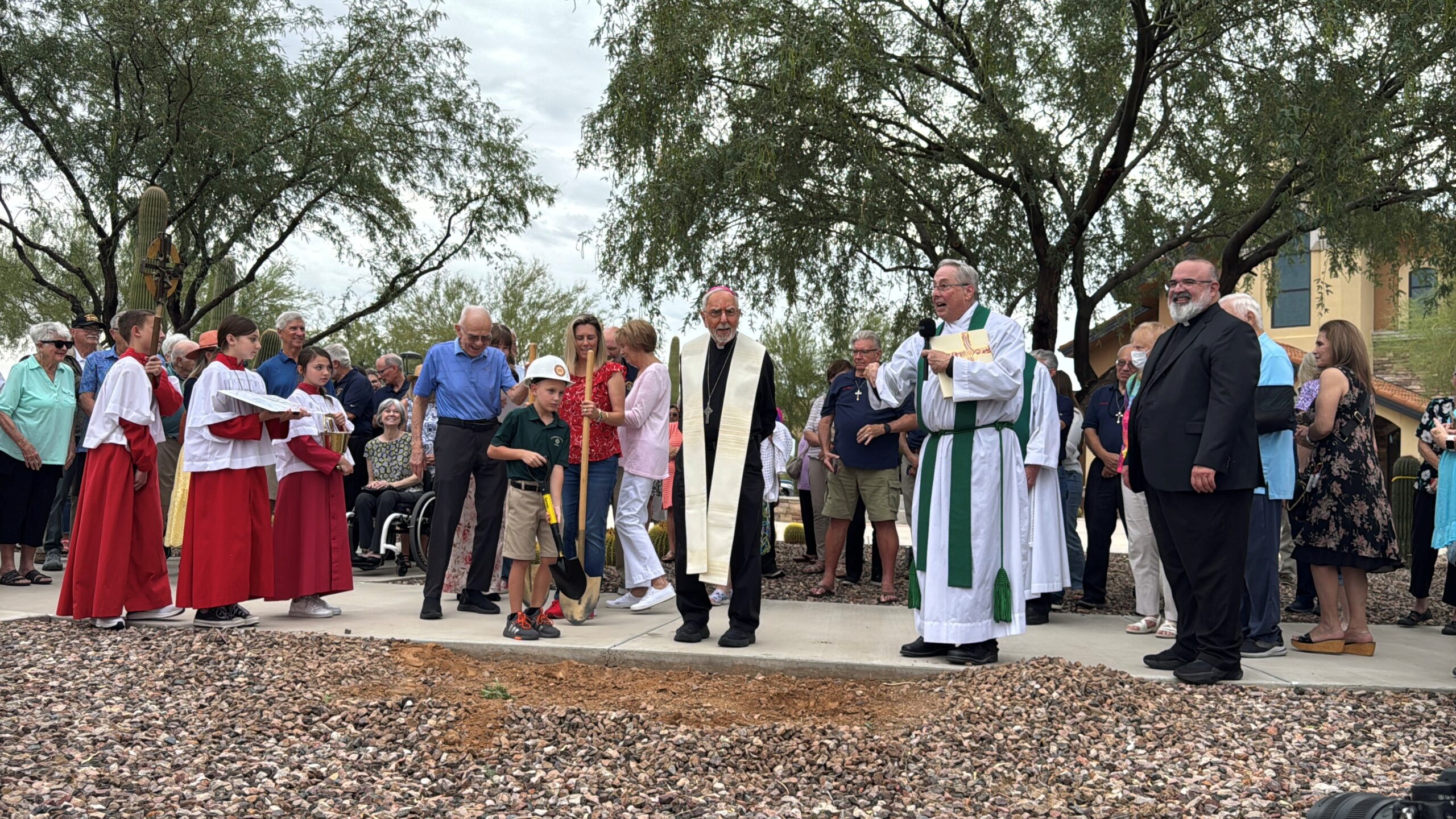 Image showing a group of people celebrating a groundbreaking event. A Bishop stands in the front blessing the site.